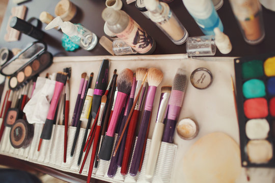Make-u brushes lie between eye-shadows and tools on a table