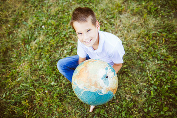 teenager boy holding a globe in his hand sitting on the grass , outdoors