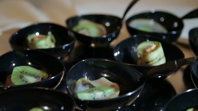 Particolare di piccole ciotole nere con cibo antipasto e buffet servito in un ristorante. Kiwi. 
