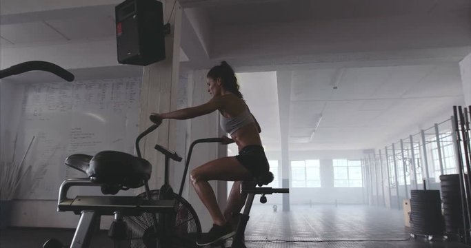 Sportswoman using air bike at the gym. Fitness female doing cardio workout on stationary cycle at gym.
