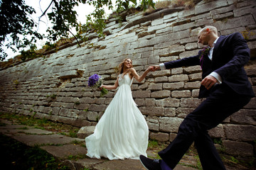 A wedding couple dance behind a stone wall