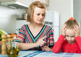 woman lecturing small female child in the kitchen