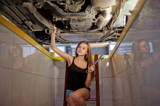 Young sexy brunette mechanic in checked shirt in car repair pit.