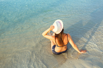 Fototapeta na wymiar Beach vacation. Young woman in a hat and bikini sitting on the b