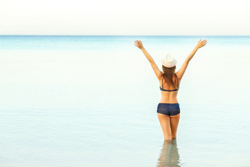 Woman in sun hat and bikini enjoying looking view of beach on su