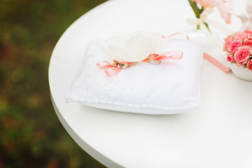 Wedding rings bound with a pink ribbon lie on a white pillow