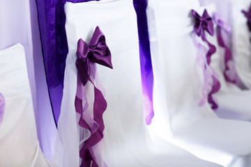 Chairs enveloped in white cloth decorated with violet bows