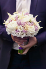 Hroom holds a tender wedding bouquet of white roses and violet l