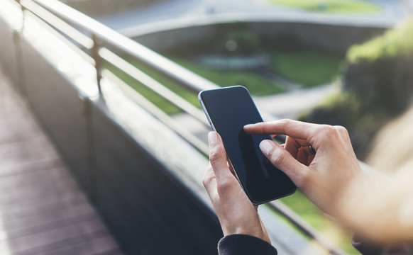 Hipster texting message on smartphone or technology, mock up of blank screen. Tourist girl using cellphone on bridge background close, blur. Female hands holding gadget. Mockup copy space for design