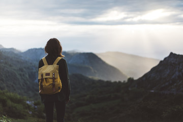 Hipster girl with backpack enjoying sunset on peak foggy mountain. Tourist traveler on background...