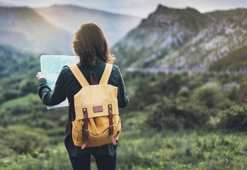 Hipster young girl with bright backpack enjoying sunset on peak mountain, looking a map. Tourist...