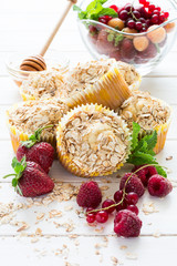 Homemade oat muffins with honey and fresh berries on white wooden background