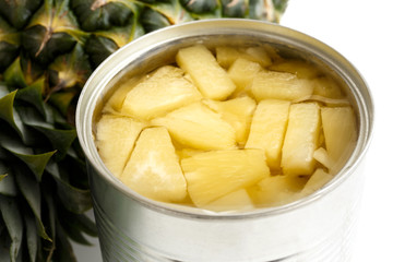 Pineapple pieces in tin on white next to pineapple.