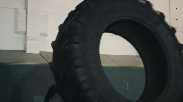 Young man lifting big wheel in bootcamp gym