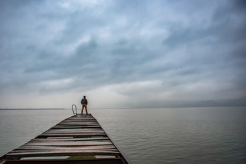 Man standing on a old wooden dock in stormy weather