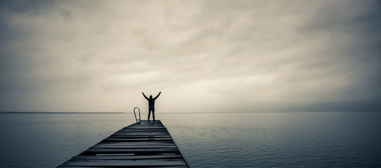 Man standing on a old wooden dock with raised hands