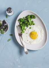 Fried egg and broccoli. Healthy breakfast or snack. On a light blue background, top view