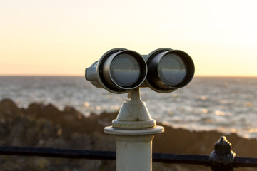 White telescope stands on sea coast in front of golden sunset