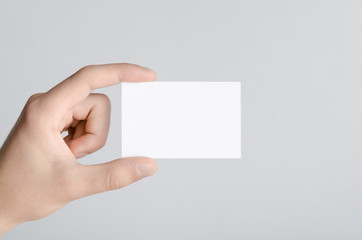 Business Card Mock-Up (85x55mm) - Male hands holding a blank card on a gray background.