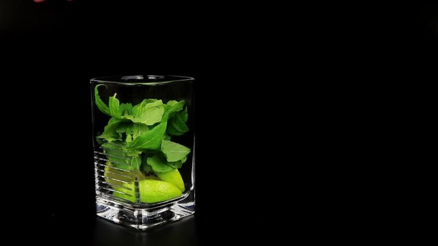 Mojito cocktail with fresh limes, mint and ice cubes on black background