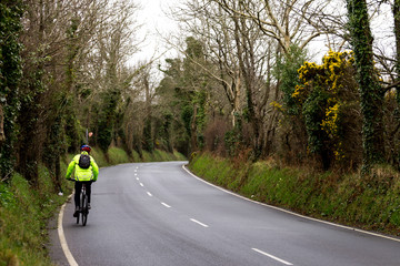 Fototapeta premium man riding a bicycle up a country road in high-visibility jacket 