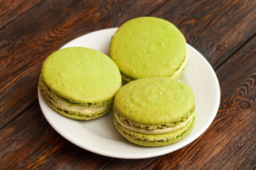 Three traditional french pistachio macarons on plate, dark wooden background