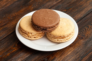 Three traditional french chocolate macarons on plate, wooden background