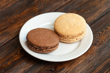 Two traditional french chocolate macarons on plate, wooden background