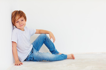 handsome young boy, kid sitting near the white wall