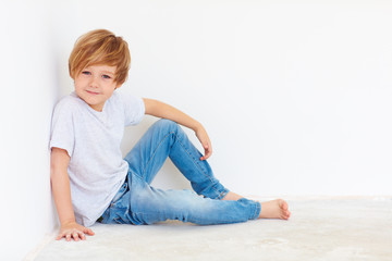 handsome young boy, kid sitting near the white wall