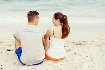 Fototapeta premium Young couple looking at each other while sitting on beach