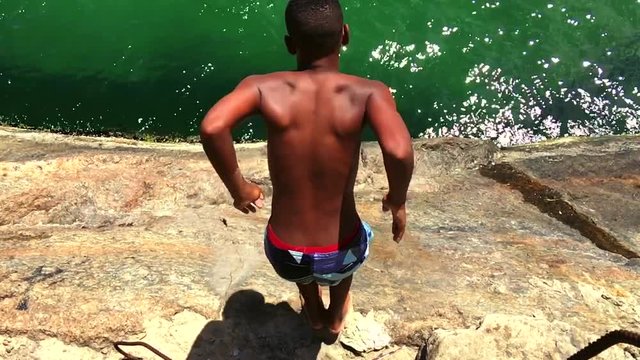 Young Brazilian man dives from a rock at the Leme end of Copacabana Beach into deep green waves Rio de Janeiro, Brazil