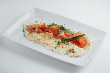 risotto with bacon, tomatoes and arugula on a white plate