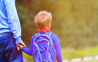 father holding hand of little son with backpack outdoors