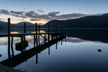 Beautiful dawn blue hour reflections at Derwentwater Lake with silhouetted jetty.
