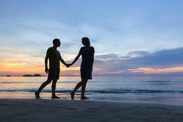 Happy romantic couple walking on the beach at sunset