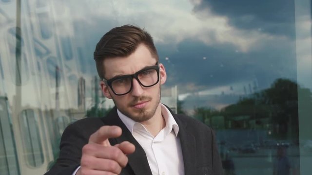 Close-up of young handsome businessman in black suit looking at camera and pointing finger at you camera gesture. Happiness, gesture, emotions concept.