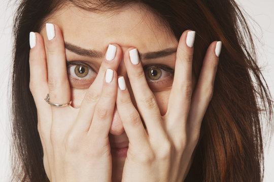 Young woman peeking through fingers as a symbol of fear