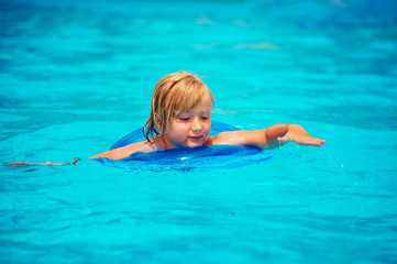 Fototapeta na wymiar Happy little boy playing in swimming pool on a hot summer day