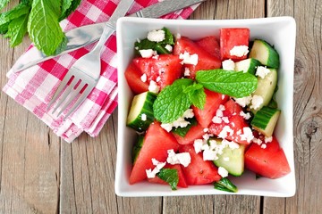 Healthy watermelon, cucumber and feta cheese salad in square bowl, overhead scene on wood background