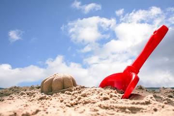 Fototapeta na wymiar red toy shovel and molded sand on the beach against the blue sky