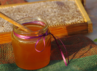 Honey in a glass jar and bee honeycombs.