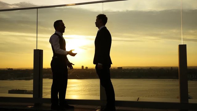 two young business man meeting on rooftop at sunset sky. talking conversation