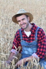 Fototapeta premium Smiley cowboy man handsome and good looking with hat, overalls and plaid shirt in rural USA countryside. Male model in american western prairie landscape nature on ranch or farm in USA.