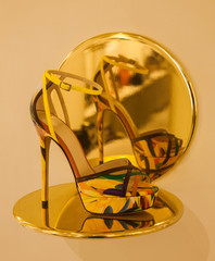 High heel shoe on a brass shelf and its reflection in a brass mirror.