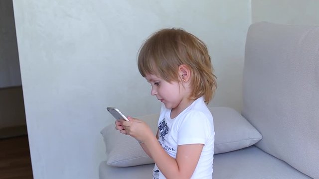 Young girl female girl woman with blonde hair white light room home office. Little girl plays on phone and smille looks to camera