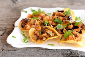 Chopped roasted eggplant with tomatoes and green parsley on potato chips. Delicious snack on a plate and on old wooden table. Tasty fried eggplant recipe. Closeup
