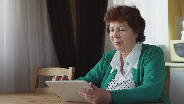 Mature woman uses a white tablet PC at home - Side view