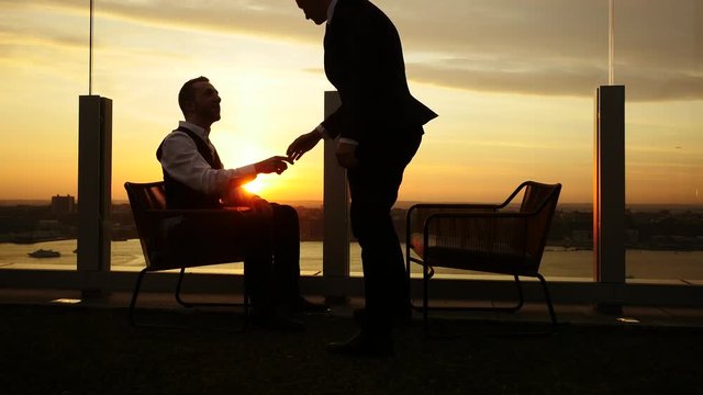 get to getter of two young businessman meeting up on rooftop at sunset light