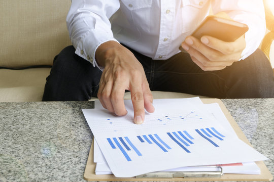 businessman holding mobile phone with analyzing financial chart